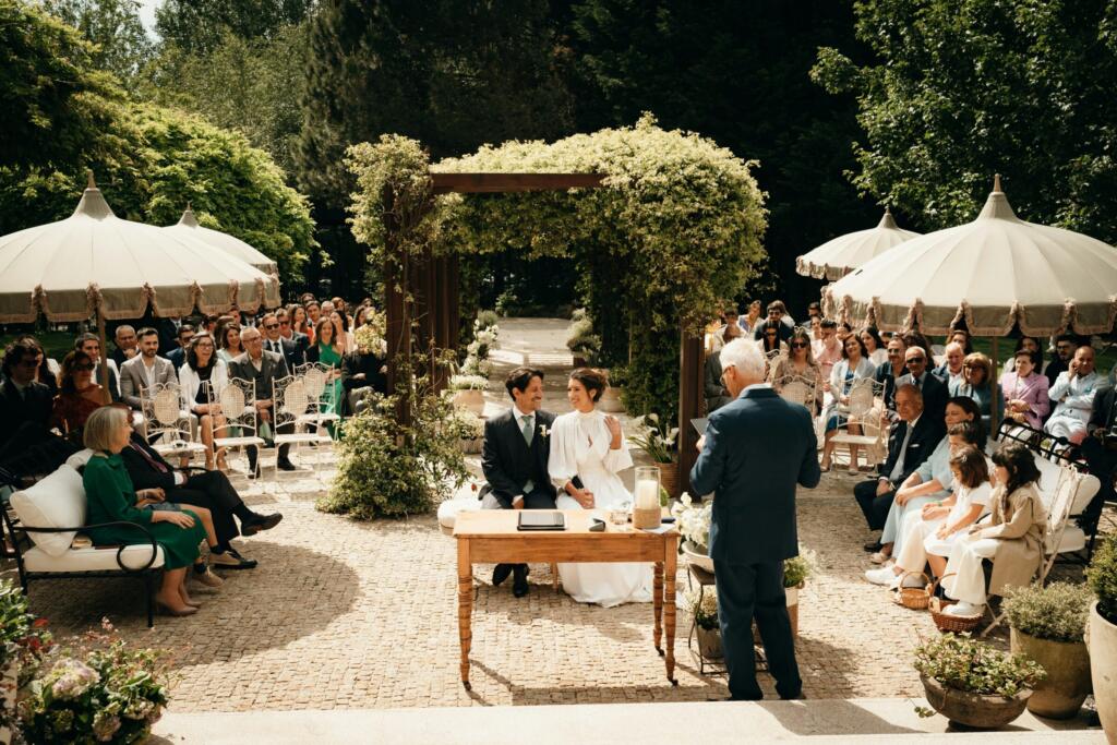 Wedding guests seated outdoors under umbrellas during a ceremony